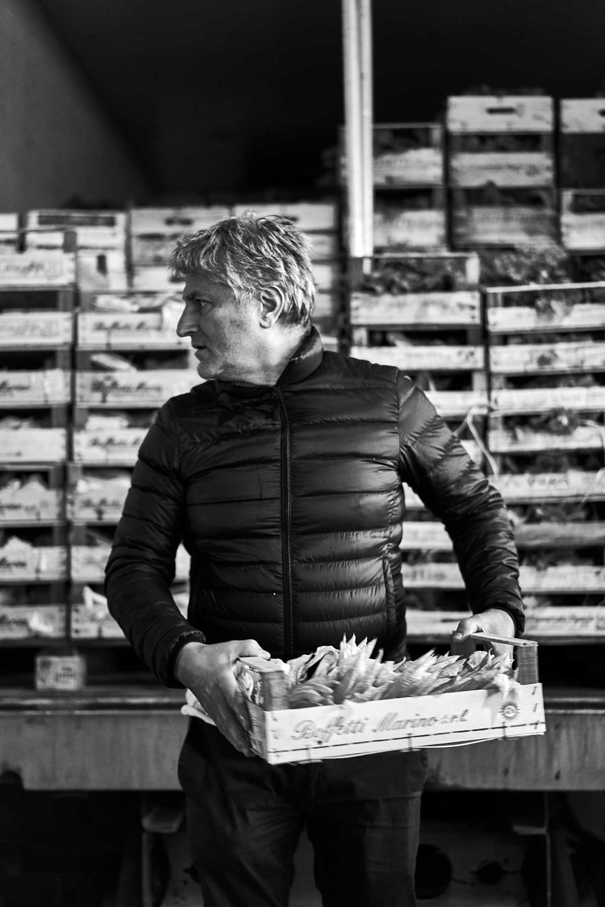 Rocco Princi holds a crate of squash blossoms in a produce market